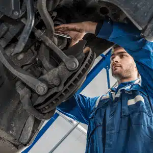 Technician in blue uniform examining land rover suspension parts near the front wheel area
