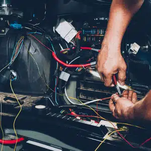 A mechanic works on repairing tangled electrical wiring inside the dashboard of a car