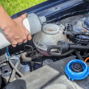 A person pours coolant into the engine reservoir to prevent overheating and maintain performance