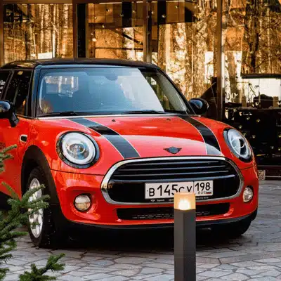 A stylish red MINI Cooper with black stripes parked near glass buildings, discussing how long do MINI Coopers last