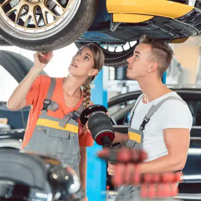 Two mechanics inspecting Land Rover air suspension on lift, discussing common land rover air suspension problems