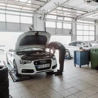 Mechanic inspects an Audi vehicle inside a service garage with hood raised during routine maintenance