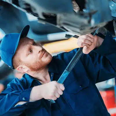 Mechanic in blue uniform repairs undercarriage while following jaguar maintenance schedule for required service intervals