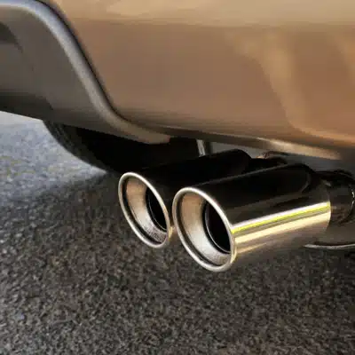 Shiny dual tailpipes under bumper; driver suspects exhaust problems causing noise, fumes, and performance issues