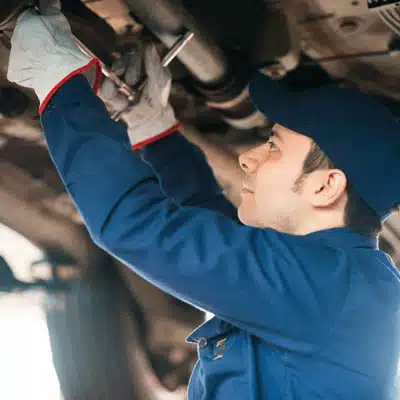 Auto technician tightens exhaust components beneath vehicle on lift, preventing leaks, rattles, and failures today