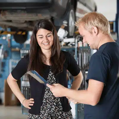 Mechanic explains repair estimate to customer in shop, reviewing maintenance plan and scheduling upcoming service