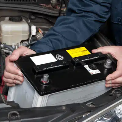 Technician lifts automotive battery from engine bay during land rover battery service at workshop today