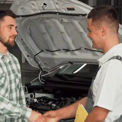Customer shakes hands with mechanic after successful car repair, standing beside vehicle with open hood