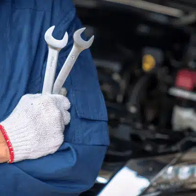 Gloved mechanic holds wrenches beside car, preparing service per volkswagen maintenance schedule at workshop guidelines