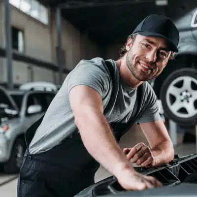 Smiling mechanic works under open hood, trusted audi specialist performing routine service in workshop today