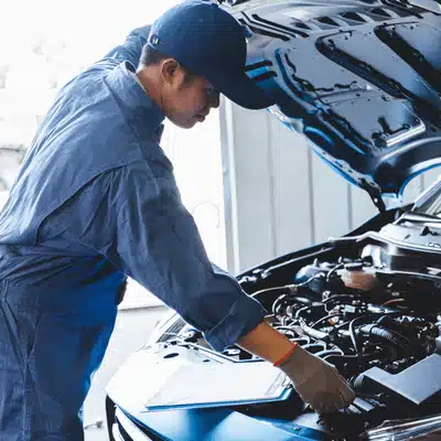 Photo shows technician leaning over car with hood raised; european car mechanic checks components carefully