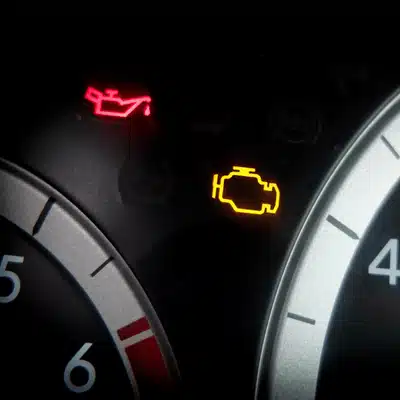 Close-up dashboard displays oil and check engine lights; jaguar repair shop identifies causes and repairs