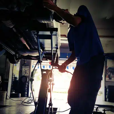 Mechanic works under raised vehicle with tools in garage while jaguar repair shop performs inspection and service