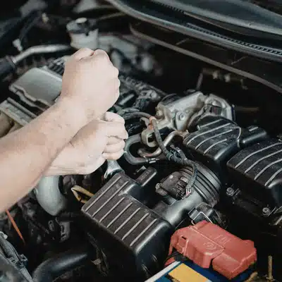 Hands use tool inside engine bay, performing checks during Land Rover service appointment maintenance visit