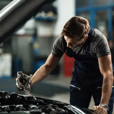 Volkswagen auto repair technician inspects engine bay under open hood while holding a shop rag
